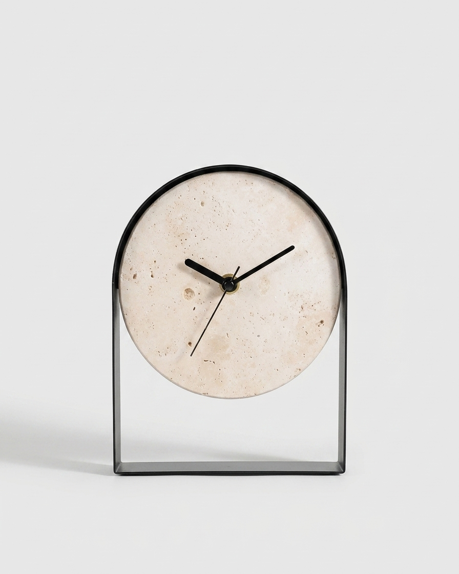 A modern minimalist tabletop clock with a circular beige stone dial and a sleek black metal frame, set against a clean light gray background.