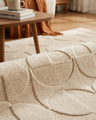 Close-up of a textured beige blanket on a couch with a wooden table and books in the background.